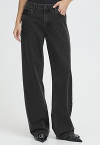 Kõrge vöökohaga mustad laiad teksapüksid pehme tekstuuriga, millel on ees taskud ja tõmblukk ning mille juurde on sobitatud terava ninaga kontsakingad.