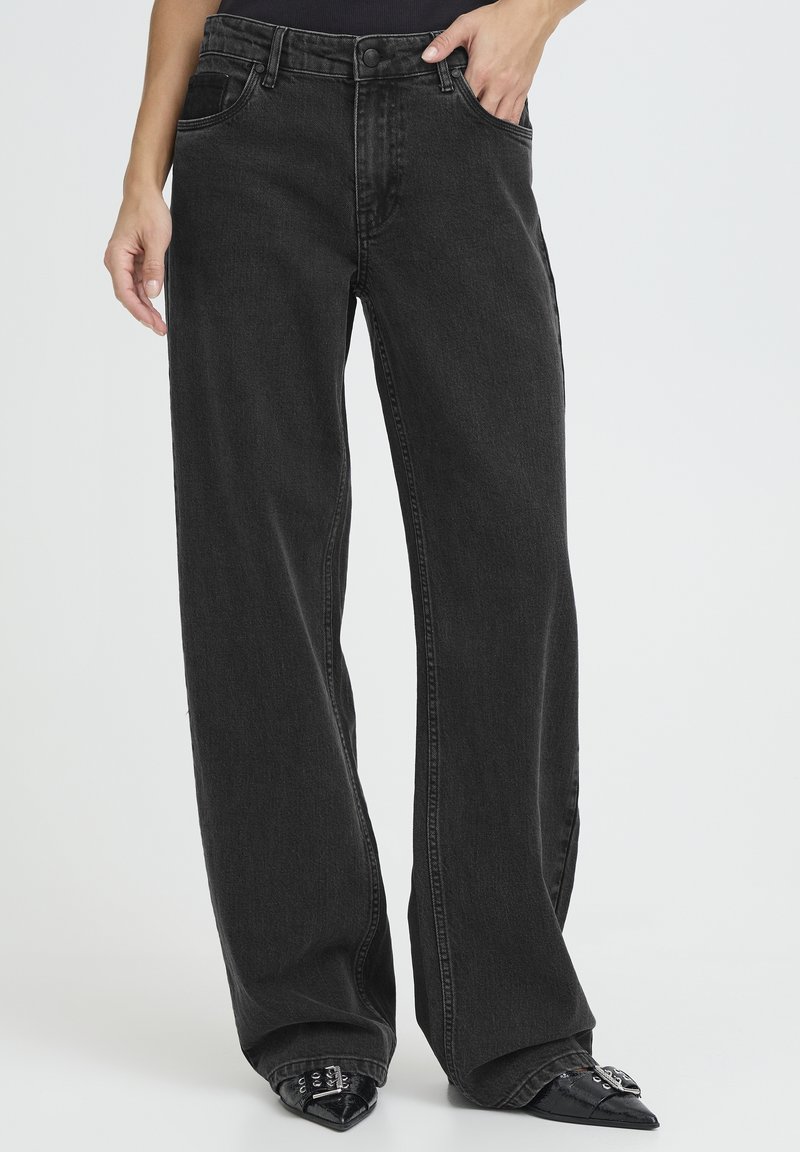 Kõrge vöökohaga mustad laiad teksapüksid pehme tekstuuriga, millel on ees taskud ja tõmblukk ning mille juurde on sobitatud terava ninaga kontsakingad.