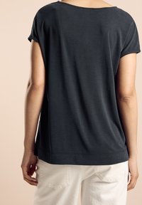 Tmavě šedé tričko s uvolněným střihem, krátkým rukávem a kulatým výstřihem. Hladká textura s jemným leskem.