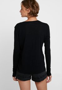 Camisa preta de mangas compridas em tecido suave e leve. Apresenta um corte descontraído e um decote arredondado, usada com calções de ganga arregaçados.