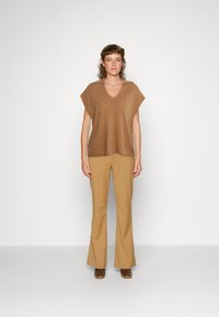 Top de malha castanho com decote em V, mangas largas, combinado com calças flare de um bege claro e sapatos castanhos. Design simples, textura suave.
