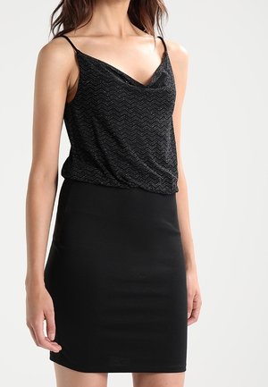 Haut noir sans manches avec une texture ondulée, superposé sur une jupe noire ajustée, créant une silhouette élancée. Tissu doux et léger.