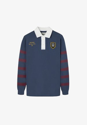 Camiseta de rugby de manga larga en color azul marino con cuello blanco. Presenta rayas rojas y azul marino en las mangas. Logo bordado en dorado en el pecho. Tejido texturizado.