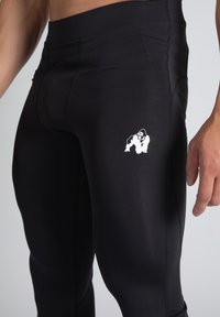 Black athletic leggings made from smooth, stretch fabric; features a white gorilla logo on the upper thigh and flat seam detailing.