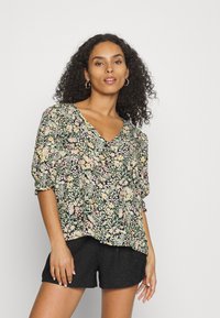 Blusa floral com decote em V, apresentando mangas curtas bufantes, fundo preto com padrões de flores coloridas. Usada com calções pretos de rendinha.