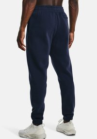 Dunkelblaue Jogginghosen aus weichem Stoff, mit einem elastischen Bund, seitlichen Taschen und schmal zulaufenden Bündchen. Kombiniert mit weißen Sportschuhen.