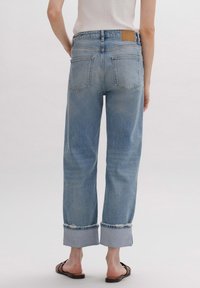 Jeans de mezclilla de color azul claro, de cintura alta y con un ajuste relajado. Presenta dobladillos enrollados, dos bolsillos traseros y un parche de cuero marrón en la cinturilla.