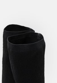 Svarta strumpor av texturerad tyg med ribbad mudd. Materialet verkar mjukt och designen är sömlös vid ankeln.