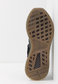 Svart idrottssko sula med en texturerad gummiyttersula, som har ett rutmönster och en gummifärgad accent nära kanten.