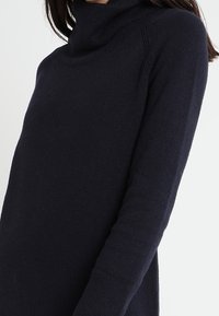 Pull à col roulé bleu marine en tissu tricot doux et extensible. Doté d'un col et de poignets côtelés, avec une coupe décontractée et des détails sur les côtés.
