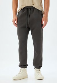 Donkergrijze trainingsbroek met een elastische tailleband en verstelbare trekkoord. Zachte textuur, taps toelopende pijpen met boorden aan de onderkant.