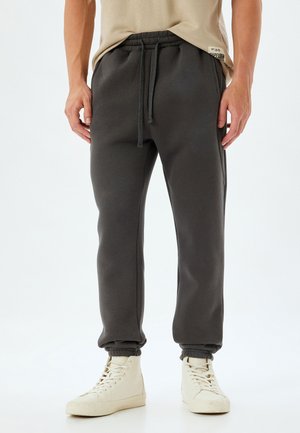 Donkergrijze trainingsbroek met een elastische tailleband en verstelbare trekkoord. Zachte textuur, taps toelopende pijpen met boorden aan de onderkant.