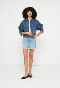 Τζιν μπουφάν σε σκούρο μπλε με σχεδιασμό καπιτονέ, συνδυασμένο με φούστα τζιν ανοιχτού μπλε με σκισίματα. Μαύρα επίπεδα παπούτσια ολοκληρώνουν την εμφάνιση.