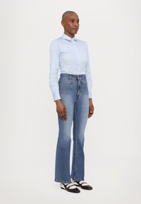 Svetlo modra srajca s kratkimi rokavi, v kombinaciji z višjimi razporek flared kavbojkami. Ima dve zadnji žepki in rob s frufrujem. Črno-bele čevlje dopolnjujejo videz.