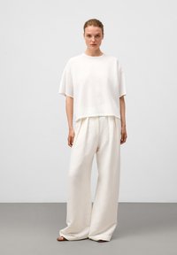Wit kortmouwtop met een ontspannen pasvorm, gecombineerd met losse witte broeken. De outfit heeft zachte texturen en neutrale tinten.
