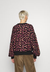 Pälsig svart tröja med ett flerfärgat leopardmönster i rosa och beige. Ribbad muddar och nederkant fulländar den avslappnade passformen.