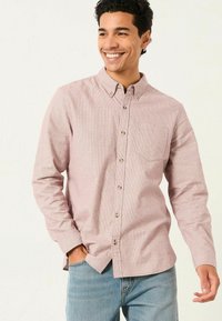 Rot-weiße karierte Langarmhemd mit einer einzelnen Brusttasche und abgerundetem Saum, kombiniert mit blauen Jeans.