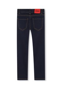 Jean skinny en denim foncé avec une texture lisse, dotés de coutures orange contrastantes, de deux poches arrière et d'une étiquette logo rouge à la taille.