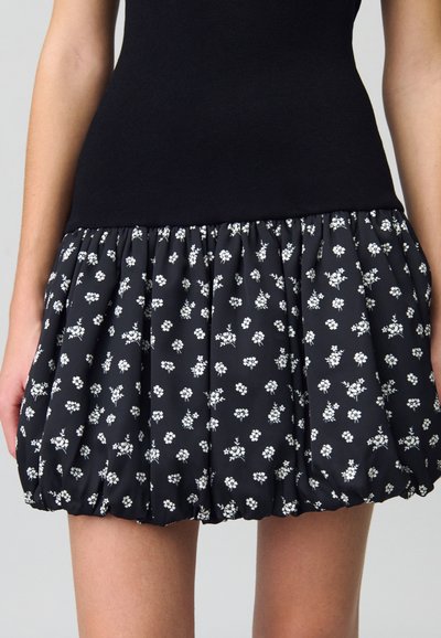 Jupe mini noire à fleurs avec une forme ballon ; présente un imprimé de fleurs blanches, une taille froncée et une texture de tissu douce.