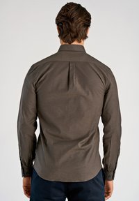 Brun skjorta med knappar framtill, lång ärm, slät textur, veckdetalj bak och knäppta manschetter. Bärs med mörka byxor.