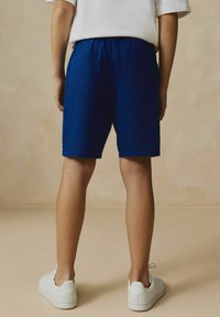 Shorts bleu à rayures avec une taille élastique, comportant deux poches arrière. Associés à des baskets blanches sur un fond neutre.