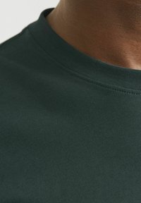 Camiseta de algodón verde oscuro con cuello redondo, que presenta un cuello acanalado y una textura suave. La vista cercana resalta los detalles del tejido.