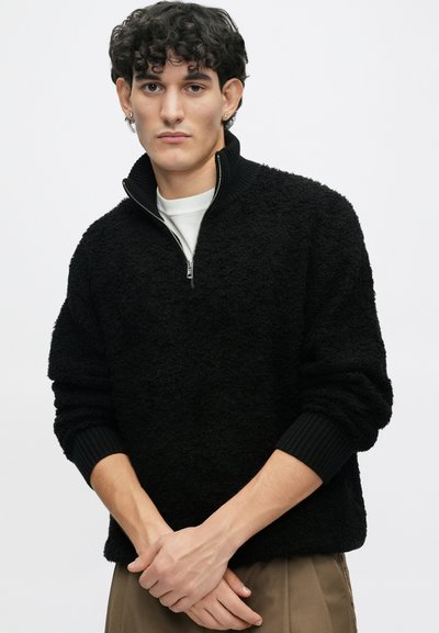 Schwarzer, strukturiertes Pullover mit einem Reißverschlusskragen und gerippten Bündchen. Weicher Stoff; lässige Passform, über einem weißen Hemd getragen.