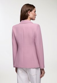 Blazer rosa chiaro con spalle strutturate, vestibilità su misura e tessuto morbido. Presenta un colletto a punta e linee pulite sul retro.