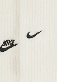 Baltas ribots zeķes ar melnu izšūtu "Nike" logo un svītru. Mīksta tekstūra ar klasisku dizainu, kas piemērots ikdienas valkāšanai.
