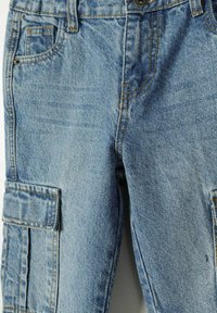 Svetlo modri denim cargo hlače z bočno žepom, vidnimi šivi in rahlo obrabljenim videzom. Prilagodljiv pas z kovinsko gumbom.