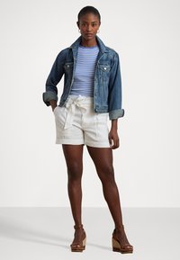 Jeans jakna s ovratnikom, modra in bela prugasta srajca, bele kratke hlače visoko pasu ter svetlo rjave espadrille z višjim podplatom.