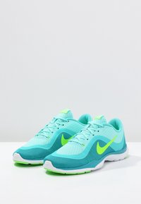 Lyseblå løbesko med grønne accenter, mesh-overdel, polstret krave og hvid gummisål. Har et fremtrædende mærke-logo på siden.