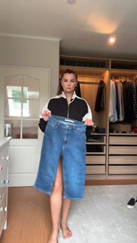 Denim krilo, modro z obreznikom spredaj, ga prikazuje oseba. Ima pas z gumbom in zanke za pas, prikazano v zaprtih prostorih.