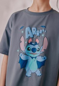 Graues T-Shirt mit kurzen Ärmeln, das eine cartoonhafte blaue Fledermaus-ähnliche Figur mit großen Ohren zeigt, umgeben von Sternen und dem Text "ARRRrrr."