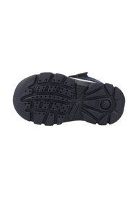 Suela de goma negra de un zapato infantil con profundos surcos, perforaciones y el número de talla 21 visible en el talón.