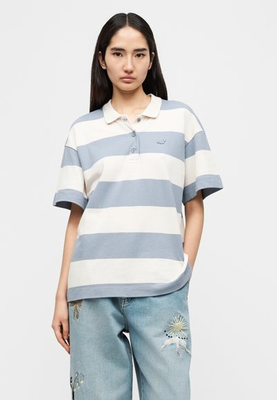 Ριγέ πόλο μπλούζα σε ανοιχτό μπλε και κρεμ, με γιακά, κοντά μανίκια και μικρό λογότυπο στο στήθος. Φοριέται με κεντημένο τζιν.