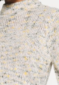 Gebreide trui met hoge hals in zachte pastelkleuren van grijs, geel en roze, met een textuur van een meerkleurig spikkelpuntpatroon.