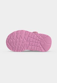 Semelle d'une chaussure rose montrant des motifs de semelle texturés variés pour l’adhérence et la stabilité sur un fond uni clair.
