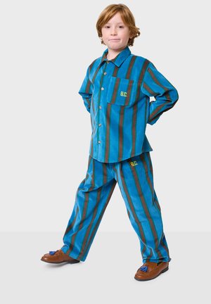 Ensemble rayé turquoise et marron composé d'une chemise à boutons et d'un pantalon assorti, avec un logo jaune sur la poche. Chaussures marron.