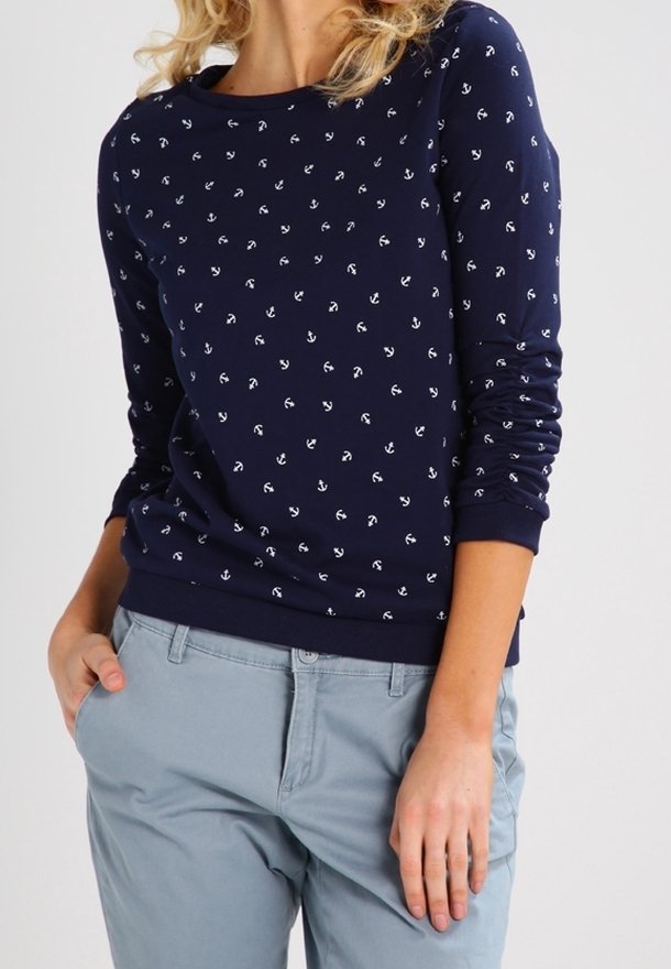 Sweatshirt bleu marine avec un motif d'ancre blanche, col rond et manches longues. Associé à un pantalon gris clair.
