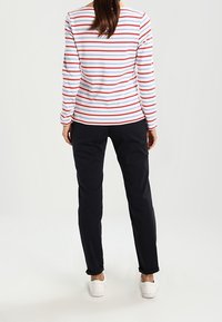 Langærmet stribet skjorte i rød, hvid og blå, parret med mørke bukser og hvide sneakers. Skjorten har vandrette striber og rund hals.