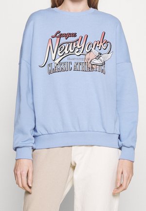Blå sweatshirt med sänkta axlar, ribbad mudd och midja. Har en djärv grafisk design med "New York" och atletiska teman.