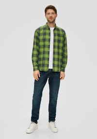 Green plaid button-up shirt with black accents, paired with a white t-shirt and dark blue jeans, finished with white sneakers.