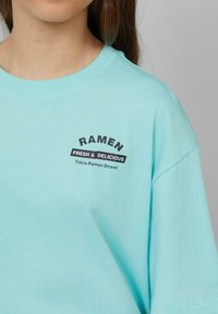 Lichtblauw korte mouwen t-shirt van katoen met een ronde halslijn. Heeft een zwart gedrukt tekst: "RAMEN FRESH & DELICIOUS Tokio Ramen Street."