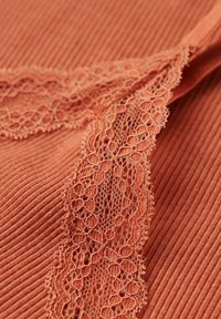 Tejido acanalado en un color terracota sutil, con un intrincado borde de encaje que realza la textura y el detalle.