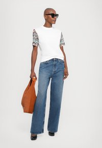 Camiseta blanca con mangas cortas de estampado, jeans de pierna ancha azules y zapatos negros. Incluye una bolsa de mano naranja. textura suave en todo.