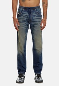 Pantalons joggers en denim avec taille élastique, couleur bleu délavé, deux poches avant et une coupe ajustée au niveau des chevilles.