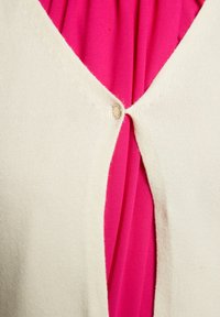 Cardigã creme com um design em V e fecho de um único botão. Por baixo, uma blusa rosa pregueada é visível. Material de malha texturizada.