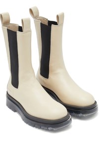Bottines Chelsea en cuir beige avec des panneaux élastiques noirs sur les côtés, des bouts ronds et de grosses semelles en caoutchouc noir. Comprend des tirants pour un enfilage facile.