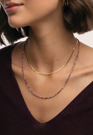 Dos collares superpuestos: una cadena delgada de oro y un collar de cuentas con cuentas multicolores en púrpura, rojo y verde.